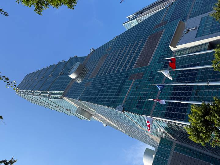 Dramatic low-angle shot of Taipei 101 skyscraper under clear blue sky with flags