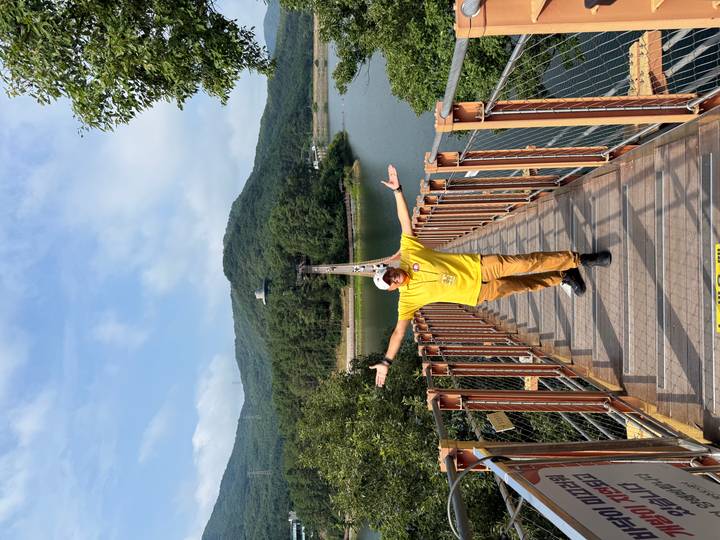 Man in yellow shirt on suspension bridge over lake with forested mountains