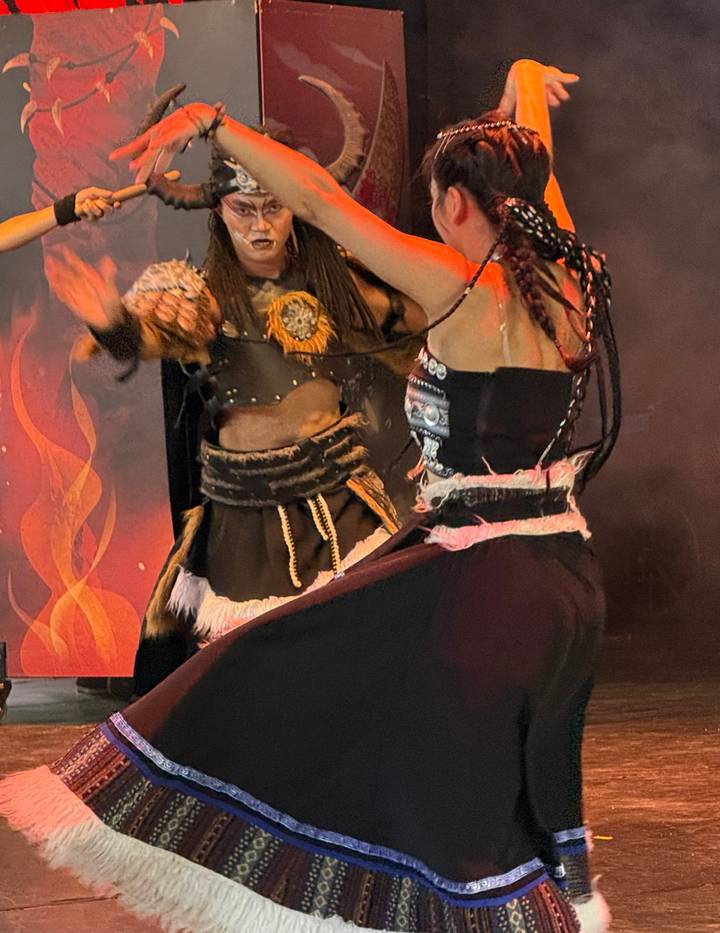 Blurry close-up of costumed performers dancing on stage with fiery backdrop