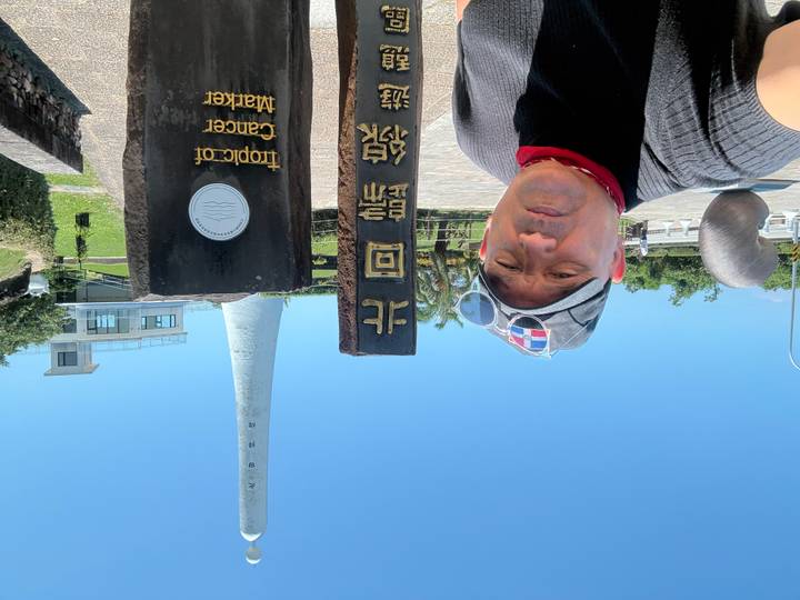 Selfie with Tropic of Cancer marker stone and tall white monument under blue sky