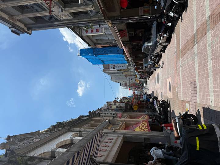 Narrow pedestrian street with scooters and shops under bright midday sun