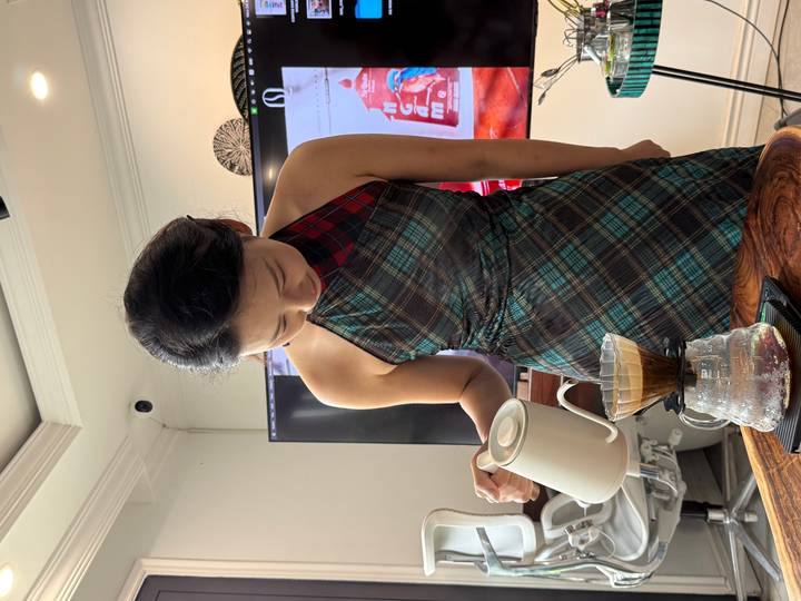 Barista in tartan dress carefully pours hot water over a filter for hand-brewed coffee
