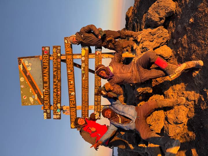 Climbers celebrate at Uhuru Peak sign with golden dawn light on the summit of Kilimanjaro