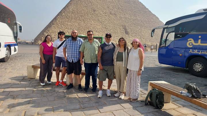 Tour group posing on a paved plaza with the Great Pyramid rising behind them