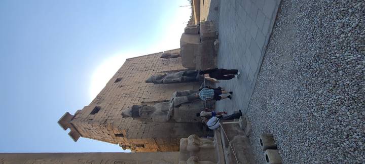 Visitors walking past colossal seated statues at Luxor Temple under bright sky