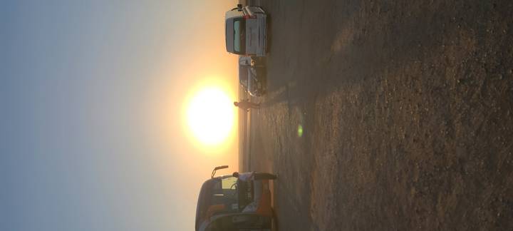 Sun setting over desert highway with parked tour buses and silhouetted travelers