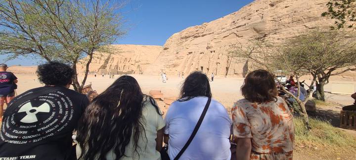 Four tourists seated on a bench gazing at the monumental façade of Abu Simbel