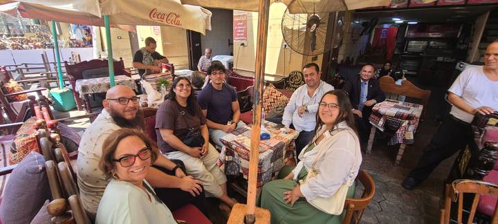 Friends gathered around patterned tables at a traditional café with fans overhead