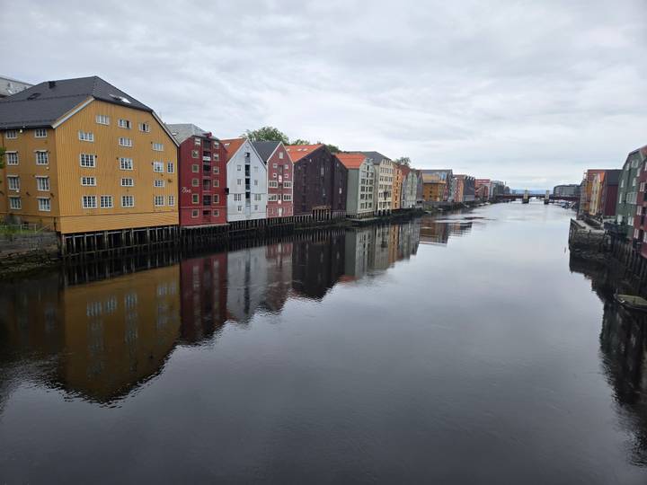 Colourful wooden warehouses line the calm Nidelva River in Trondheim under overcast skies