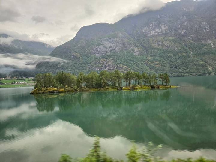 Small forested island sits in a misty green lake surrounded by towering mountains
