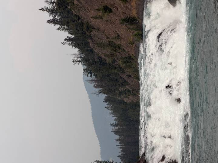 Powerful waterfall cascades through rocky terrain with forested hills in the background