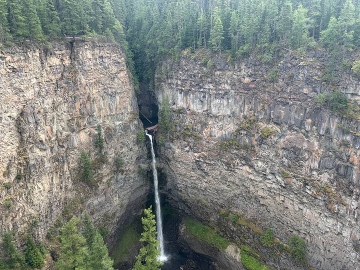 Tall narrow waterfall plunging into a deep rocky canyon lined with sheer cliffs and topped with evergreen forest.