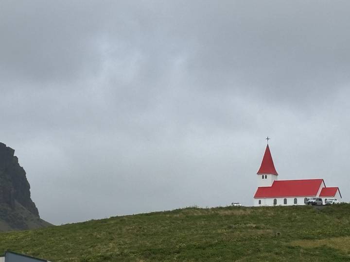 Small white church with a bright red roof and spire standing alone under a grey sky.