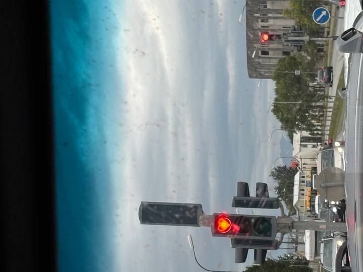 View through a car windshield toward a traffic light and urban street, with dirty glass spots visible.