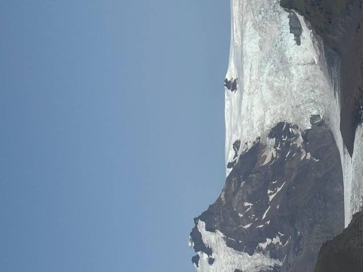 Snow-covered glacier plateau backed by dark jagged peaks under a clear blue sky.