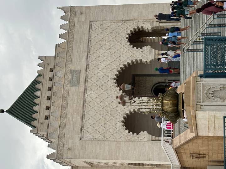 Facade of the Mausoleum of Mohammed V with ornate arches and visitors climbing steps.