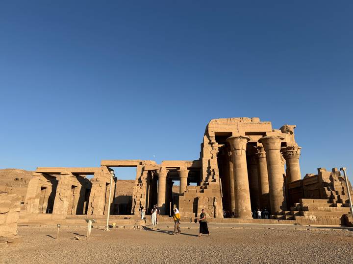 Ruins of Kom Ombo Temple with towering sandstone columns silhouetted against deep blue sky.