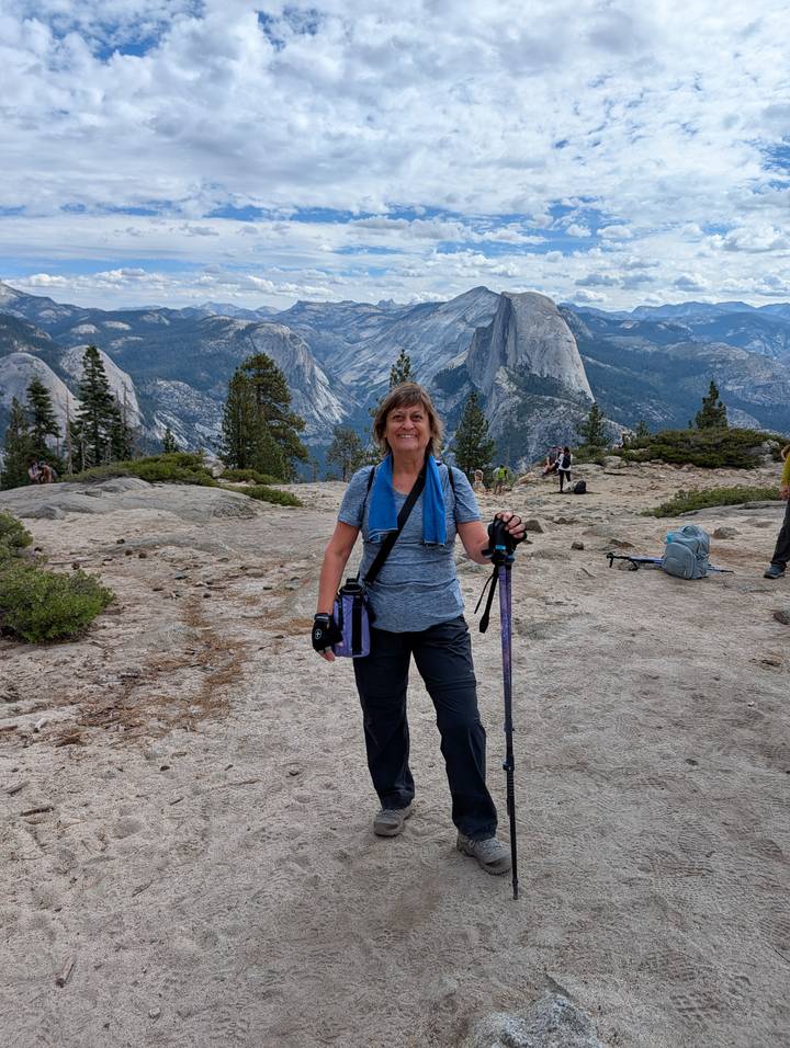 Hiker smiling on granite lookout with Half Dome and Yosemite high country behind.
