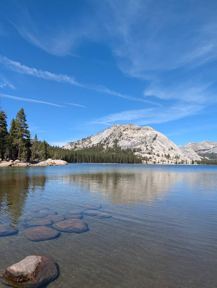 Crystal lake reflecting granite dome and pine forest beneath bright blue Yosemite sky.