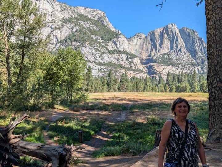 Visitor standing in meadow with towering Yosemite Valley cliffs in background.