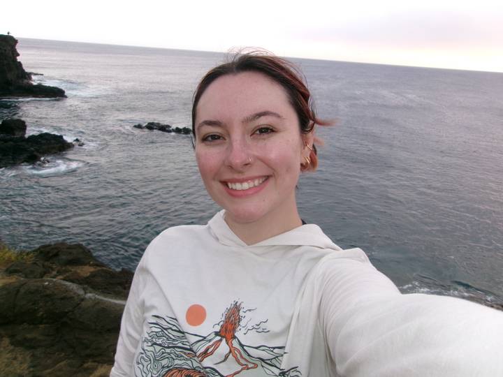 Selfie with ocean waves crashing against rugged coastline at dusk.