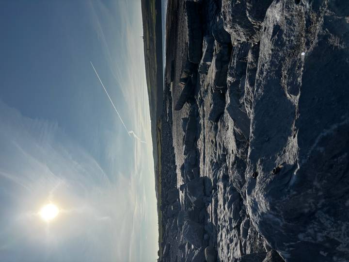 Rocky coastal landscape under low sun with jet trail across the sky.