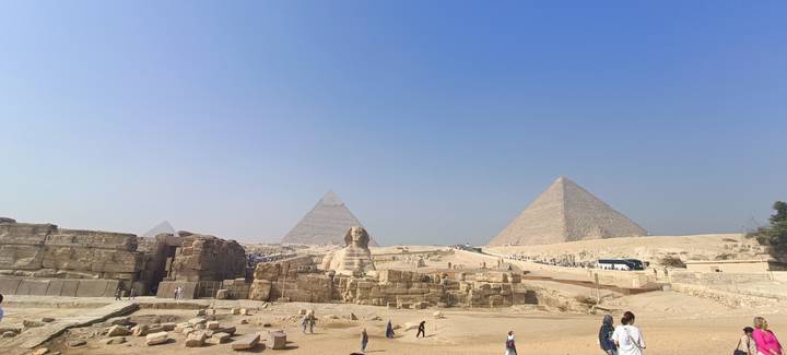Panoramic view of Giza Plateau with Great Pyramids, Sphinx and scattered tourists.