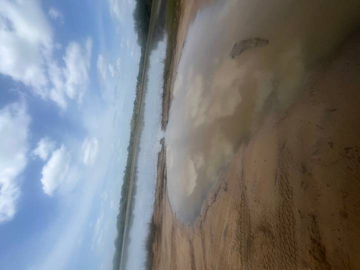 Blurry view of a sandy bank and shallow water lagoon under a partly cloudy sky.