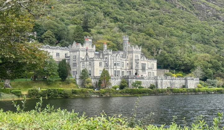 Victorian-era Kylemore Abbey reflected in a lake, surrounded by lush forested hills.