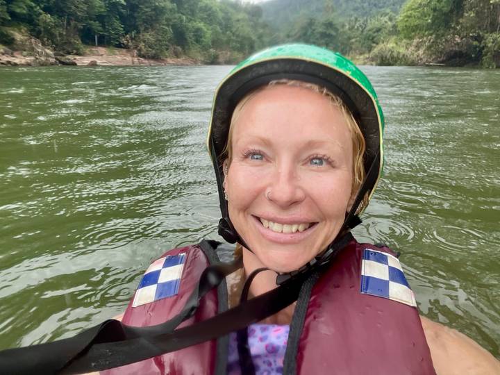 Smiling woman wearing a helmet and life vest floating in green river water during a rafting adventure.