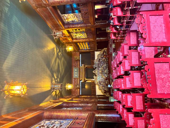 Ornate wooden theatre hall with rows of red chairs and golden lanterns inside Hue’s citadel.