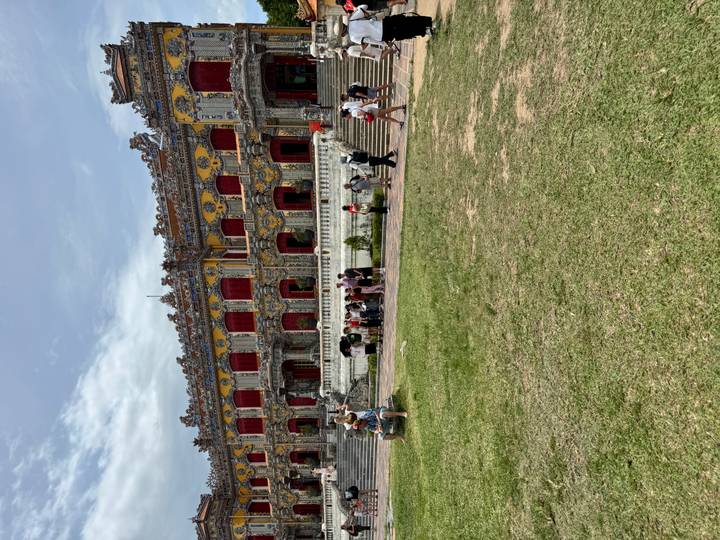 Tourists exploring expansive lawn and ornate façade of Hue Imperial Palace on a cloudy day.