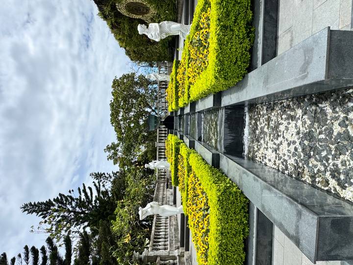 Symmetrical garden with stone water channel and manicured yellow hedges lined by statues.