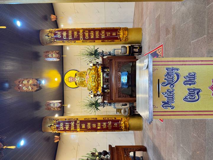 Indoor Buddhist shrine with golden statue, offering table and decorative columns.
