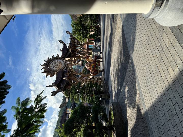 Artistic wooden sun-shaped gate structure leading into plaza under blue sky at Ba Na Hills.