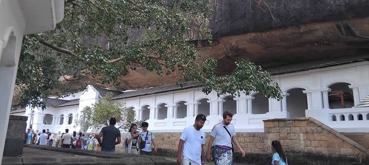Crowds explore the white-walled Dambulla cave temple complex built beneath an overhanging rock.