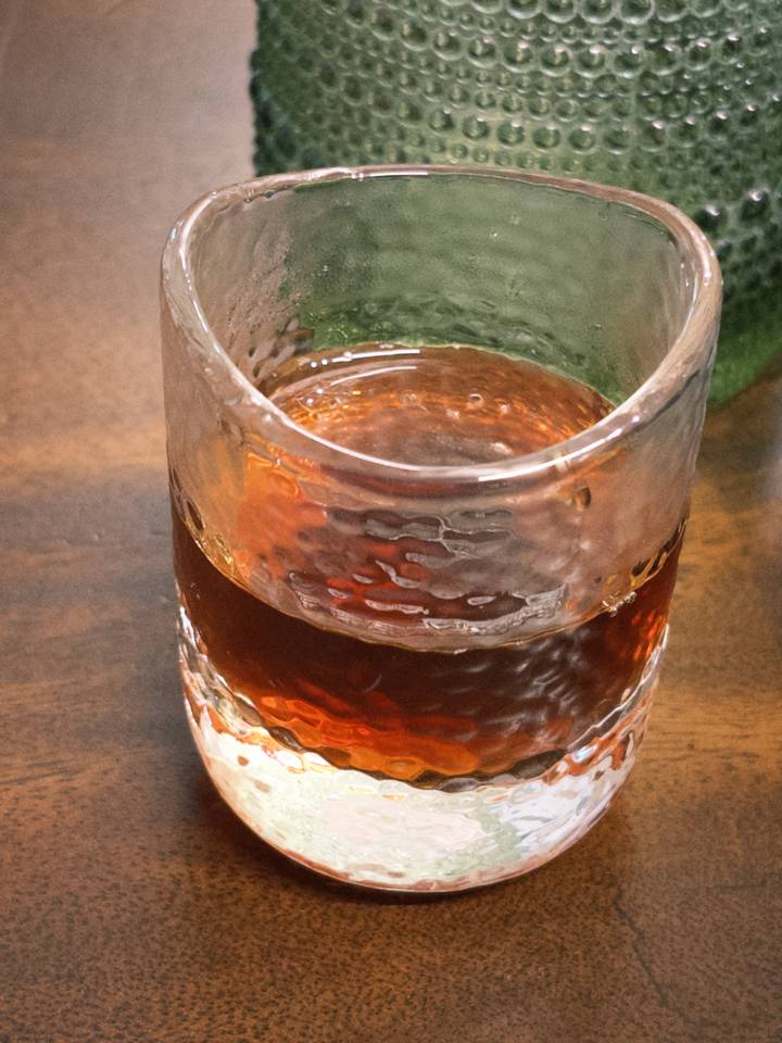 Textured glass containing dark brewed coffee placed on a wooden surface.