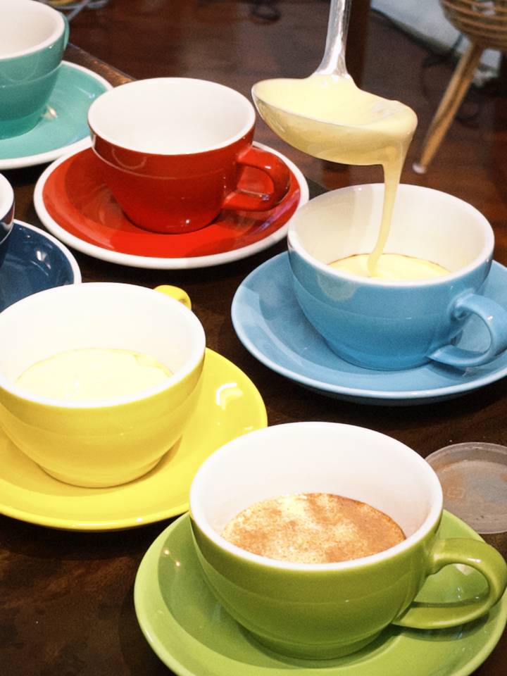 Brightly colored cups with creamy coffee being poured into a blue mug.