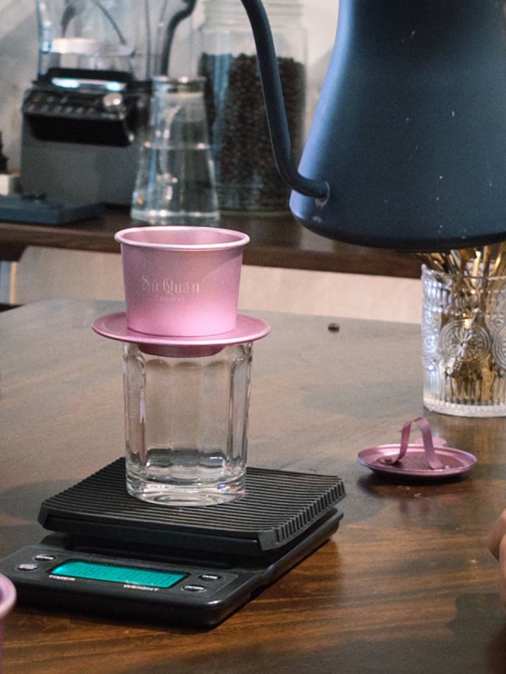 Traditional pink Vietnamese phin filter perched on top of a glass waiting to brew coffee.