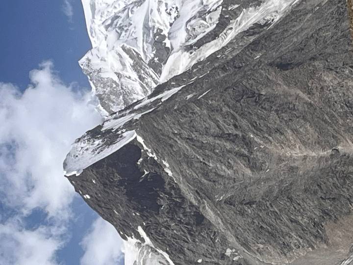 Sharp, jagged snow-capped peak rising into a blue sky with wisps of cloud.