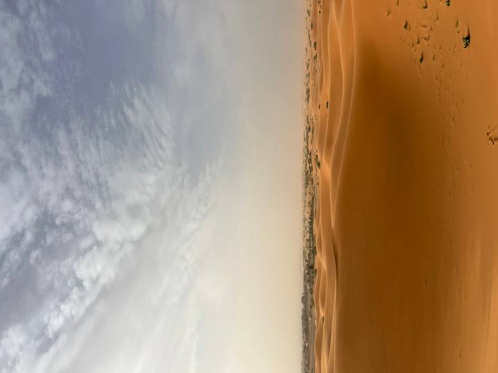 Expansive orange sand dunes under a soft, cloudy sky in the Moroccan Sahara.