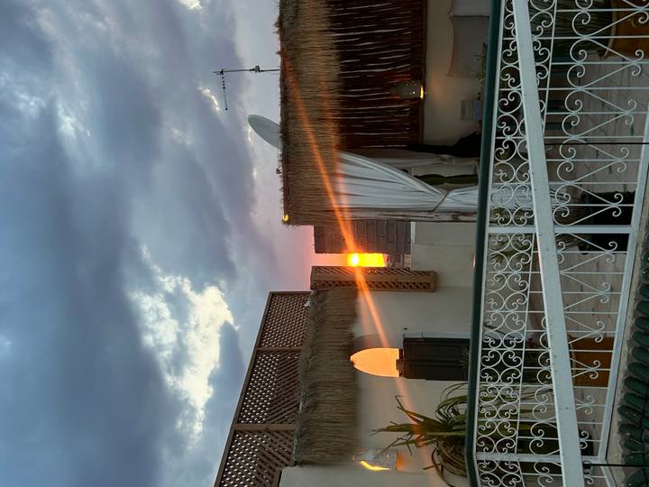 Sunset glow peeking between rooftops of a riad terrace adorned with latticework and curtains.