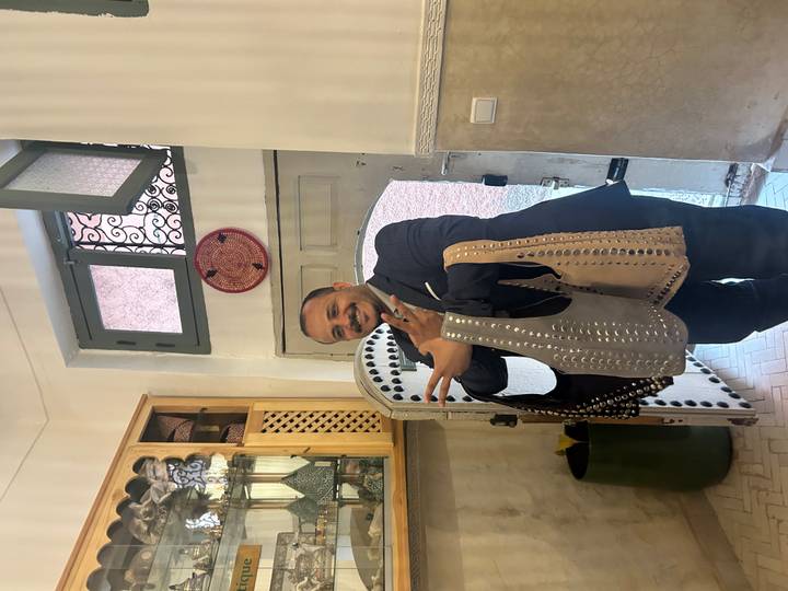 Shopkeeper proudly displaying studded leather handbags inside a traditional riad-style boutique.