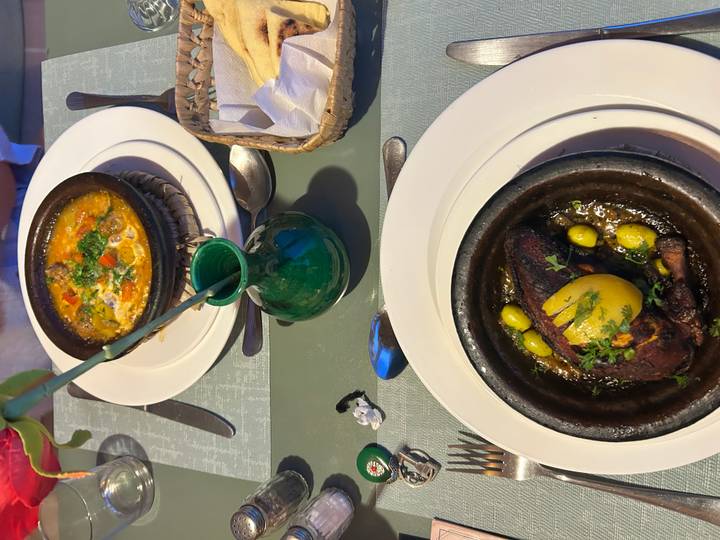 Two sizzling Moroccan tagine dishes garnished with olives and herbs served on elegant dinnerware.