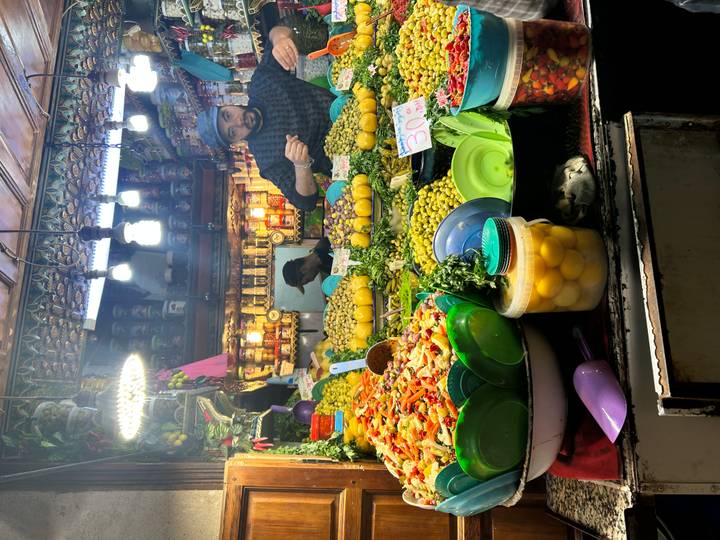 Bustling olive and preserved-lemon stall in a Moroccan souk, brimming with vibrant produce under bright lamps.