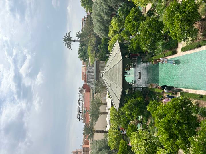 Elevated view over a lush garden courtyard with turquoise pathways and a shaded pavilion.