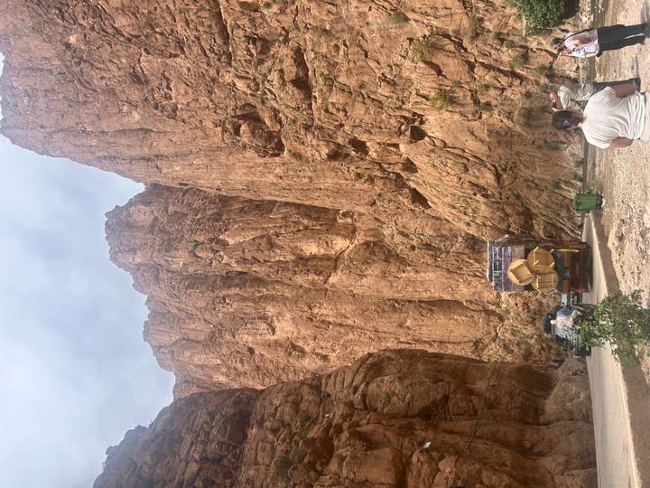 Vehicles and visitors dwarfed by towering reddish canyon walls in a dramatic gorge.