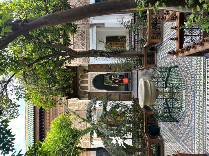 Beautifully tiled riad courtyard with central fountain framed by orange trees and intricate Moorish doorways.