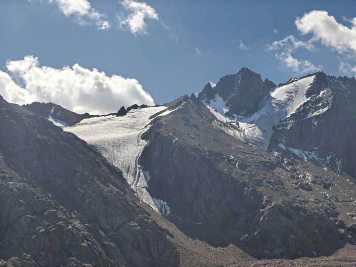 Close-up of rugged, snow-topped mountain peaks and a hanging glacier beneath a bright sky.