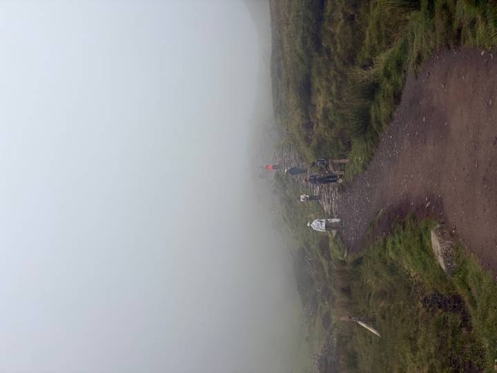 Hikers ascend a stone path that disappears into dense mountain fog.